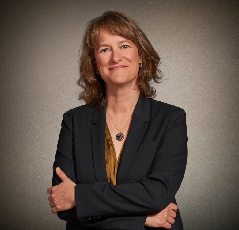 Portrait of a smiling woman in a blazer, her arms folded over her chest.