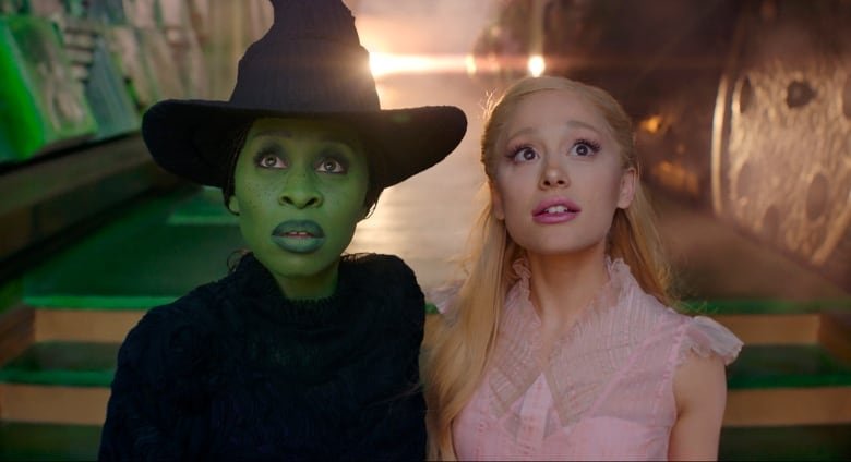 A woman with green skin and a woman wearing pink stand next to one another.