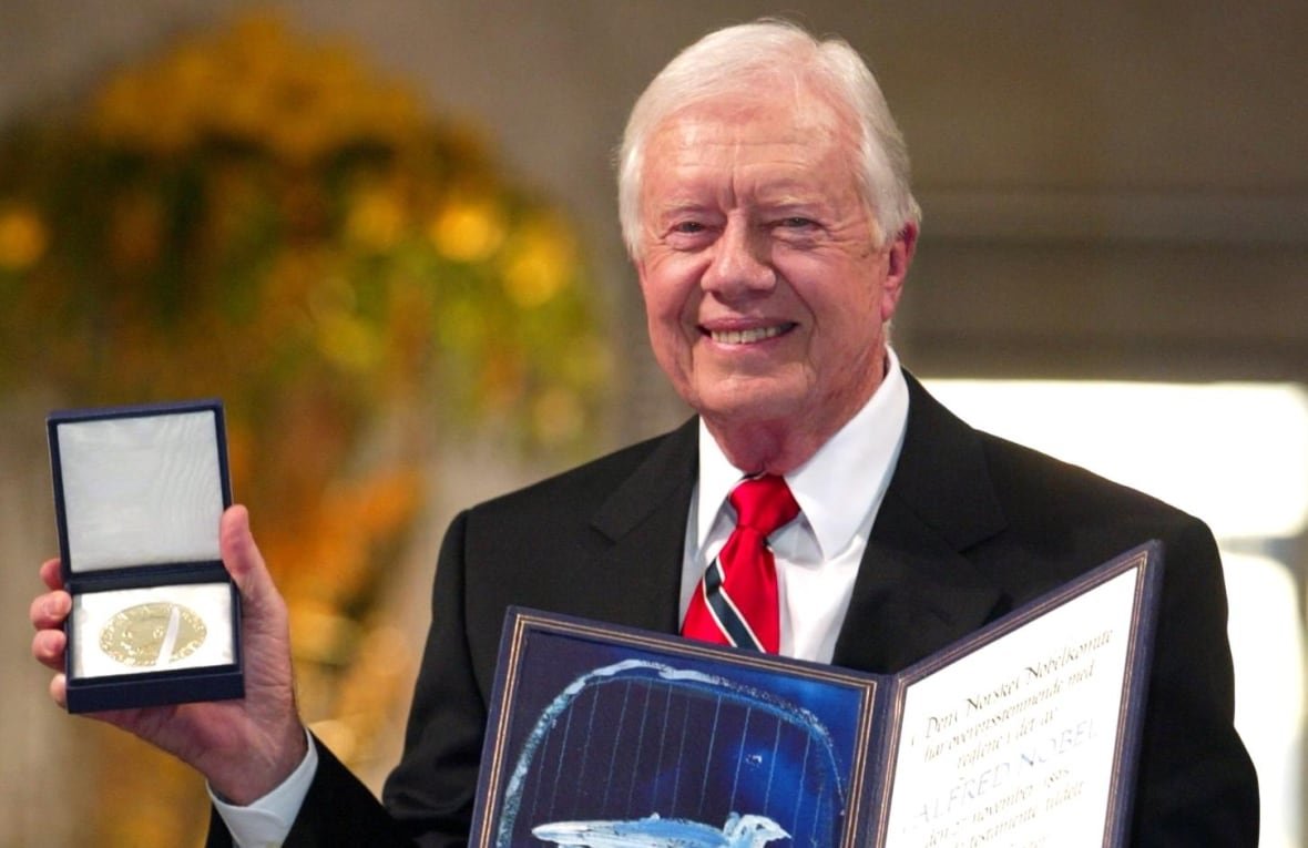 app2002121002159 Wearing a dark suit, Jimmy Carter smiles while holding his Nobel Peace Prize.