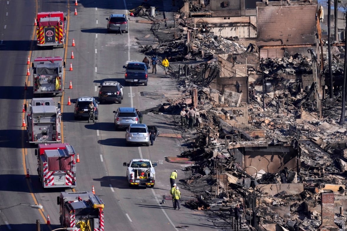 Fire trucks and other vehicles are seen parked on a road as officials work near destroyed buildings along the route.