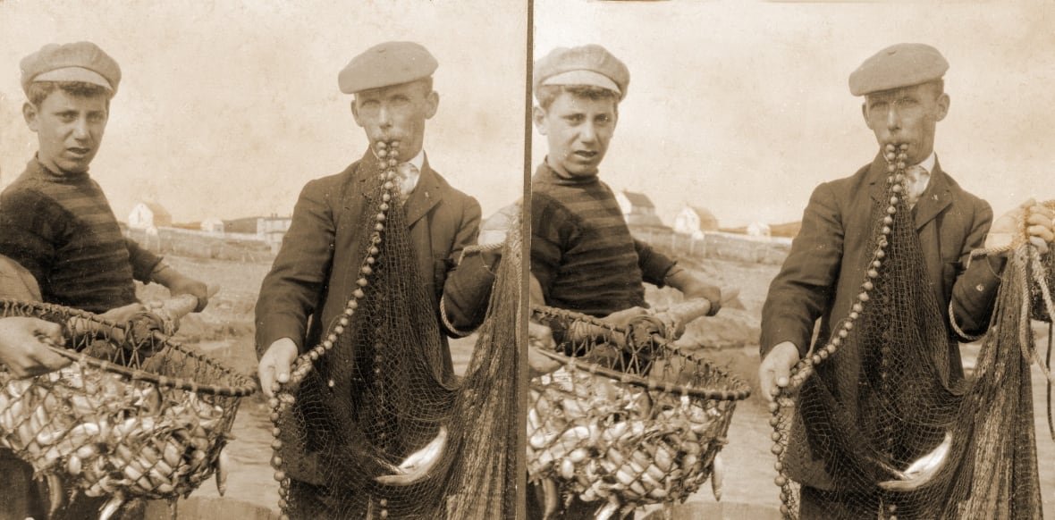 One boy stands beside another boy holding a weighted cast net in his mouth.