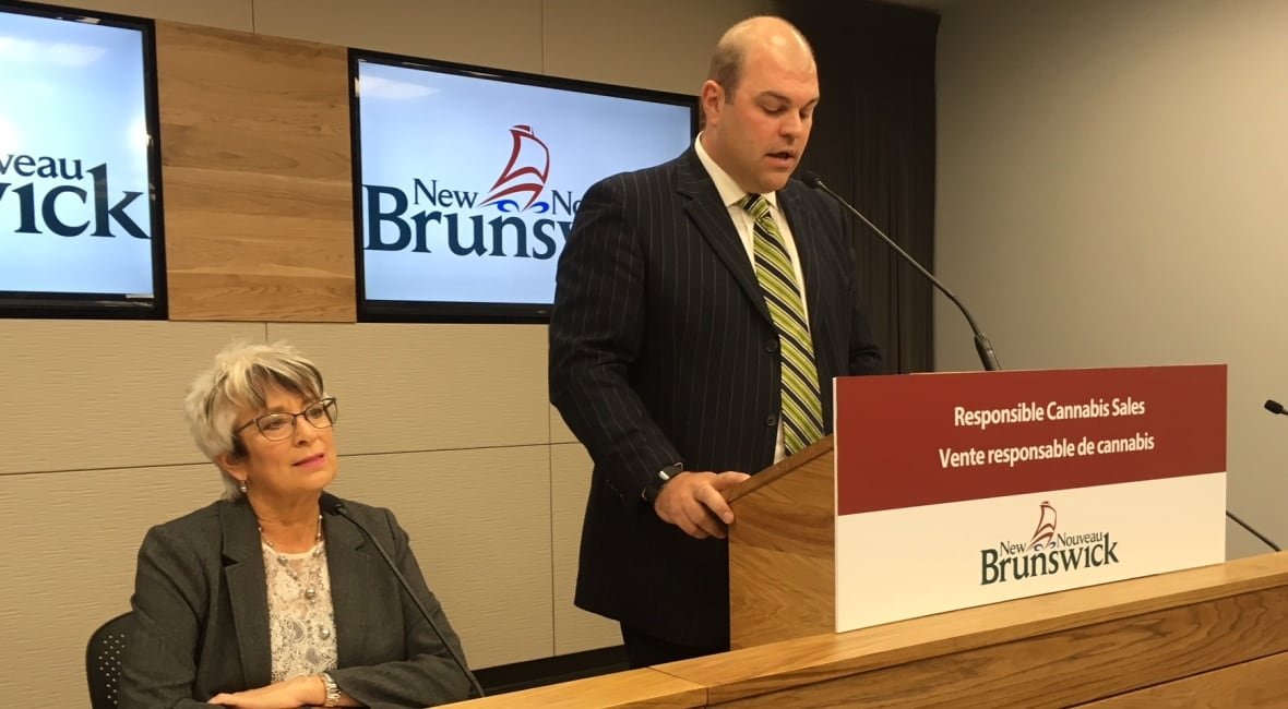 brian-harriman A man speaking at a podium. A woman sits beside him.