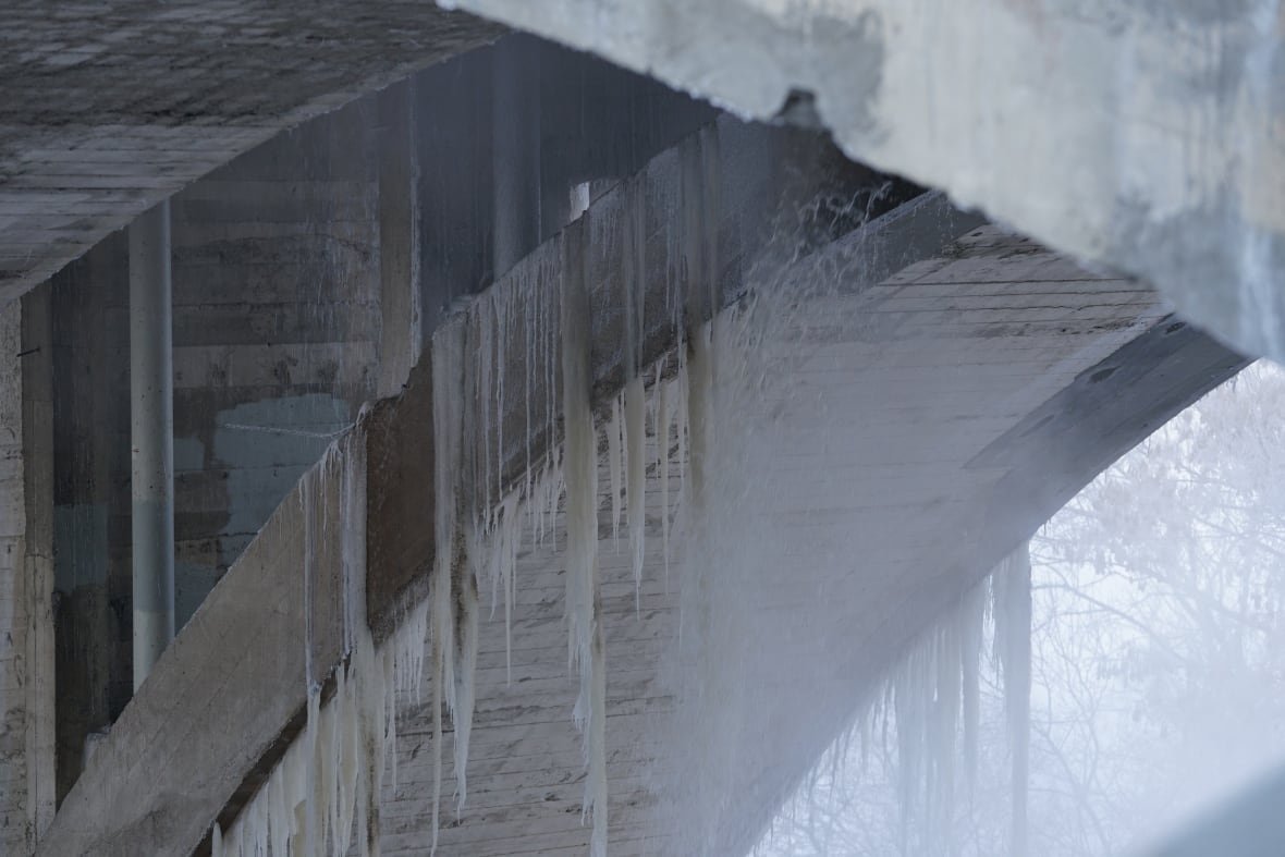 A close up of many large icicles dangling from the underside of a bridge on a cold day.