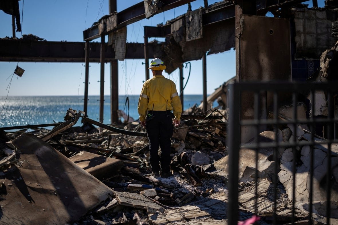 A firefighter stands amid the rubble of a destroyed building.