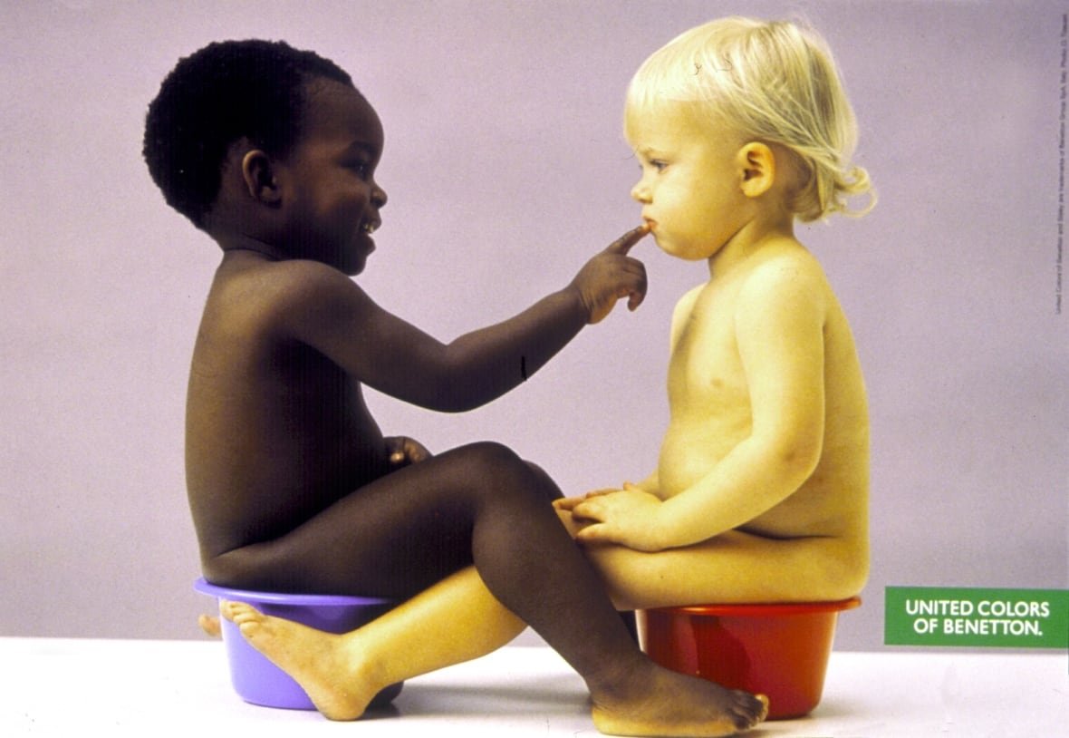 children-on-the-pot-benetton-1990 Two young naked boys are shown sitting on portable toilets. A dark complected baby touches the lips of a Caucasian-appearing baby.