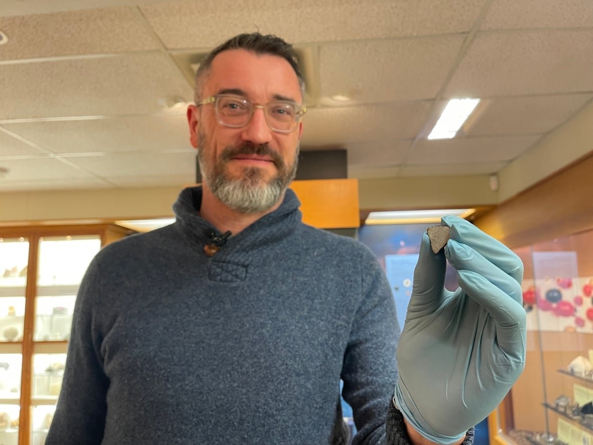 chris-herd A middle-aged man with a beard wearing a blue sweater holding a triangle-shaped rock