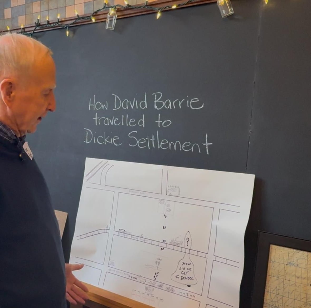 A man standing in front of a chalkboard and a hand-drawn map