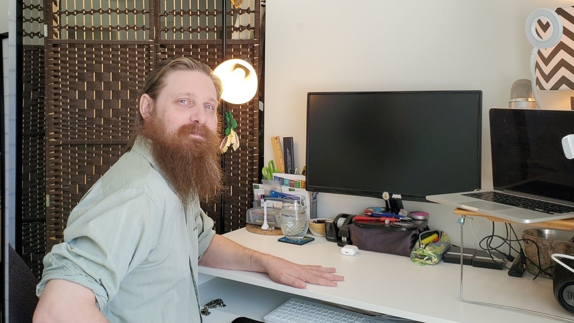 david-brown A man with a long beard sits at a desk with double computer monitors