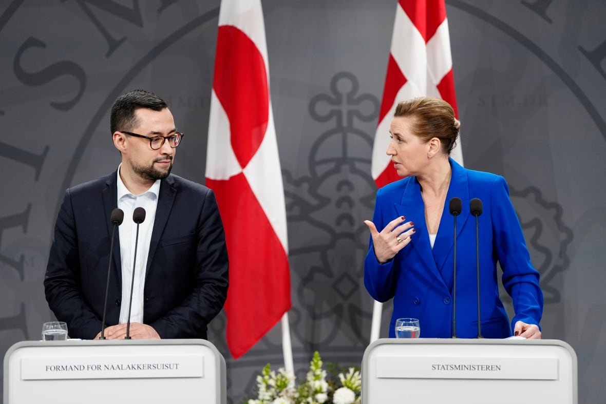 Two people stand at podiums, looking at each other.