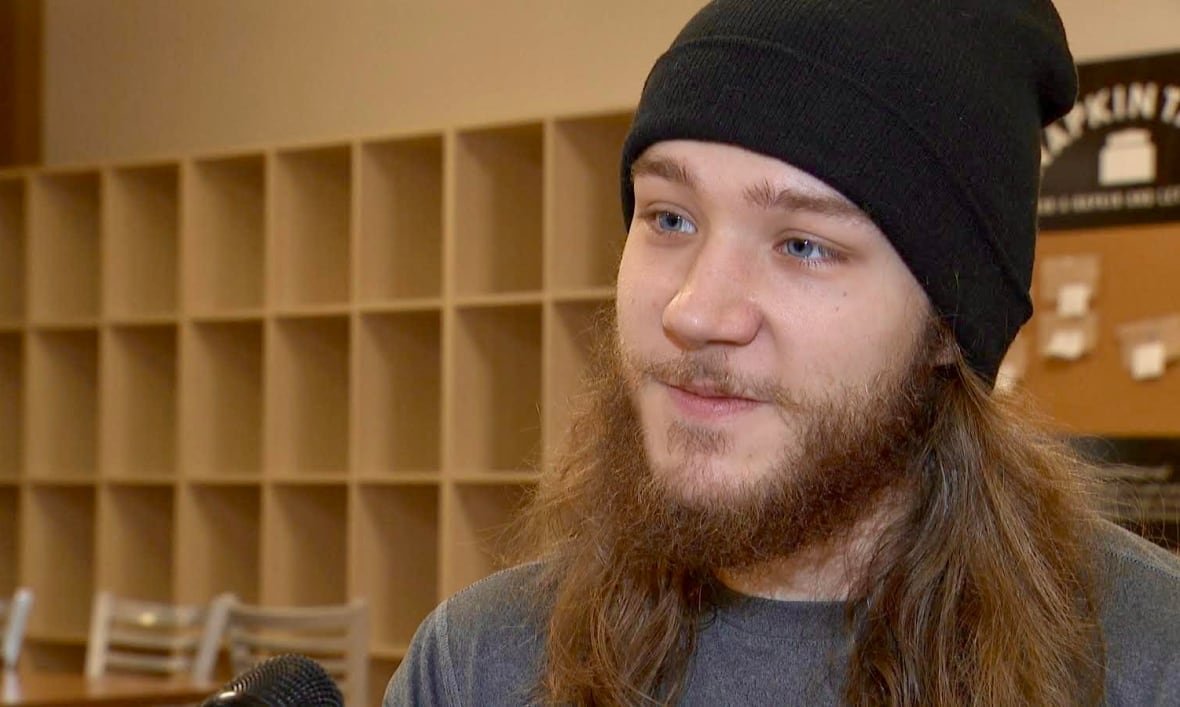 draven-harrison A man with long brown hair, a beard and a black hat, looks to the side with a slight grin on his face.