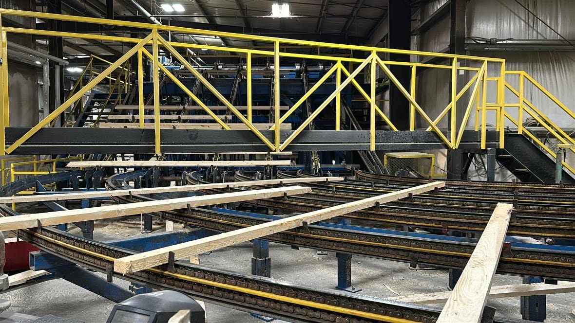 A conveyer like machine is shown moving pieces of wood such as two-by-fours that have just been cut from logs.