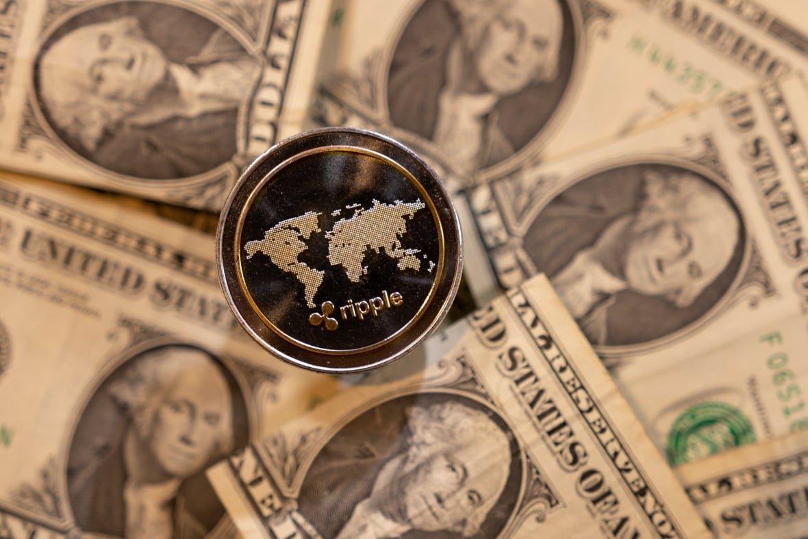 fintech-cryptocurrency A coin is engraved with the word "Ripple." U.S. bank notes are seen in the background.