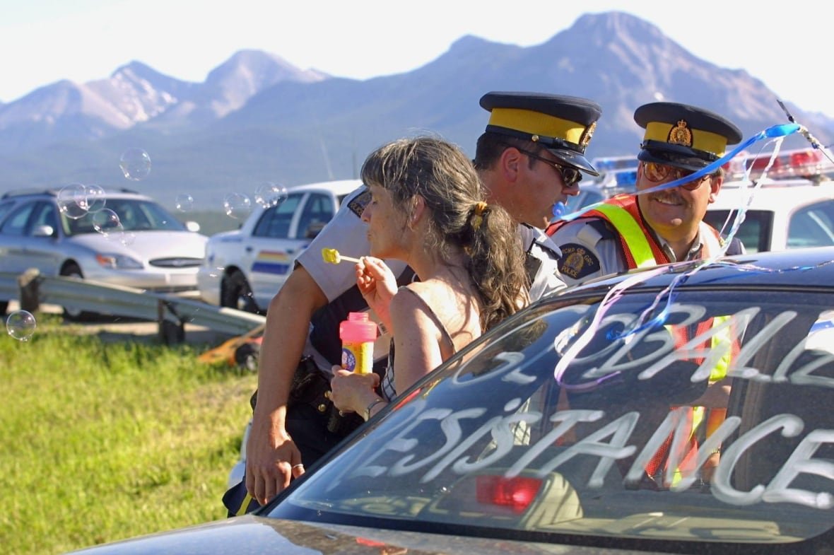 A demonstrator blows bubbles as RCMP officers speak with the driver of a car.