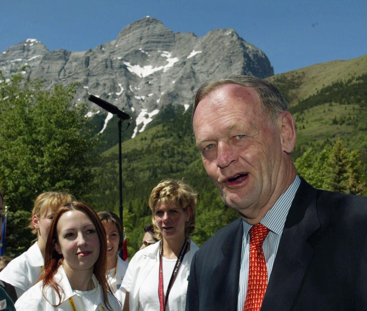 A man stands in front of a number of workers in front of a mountain.