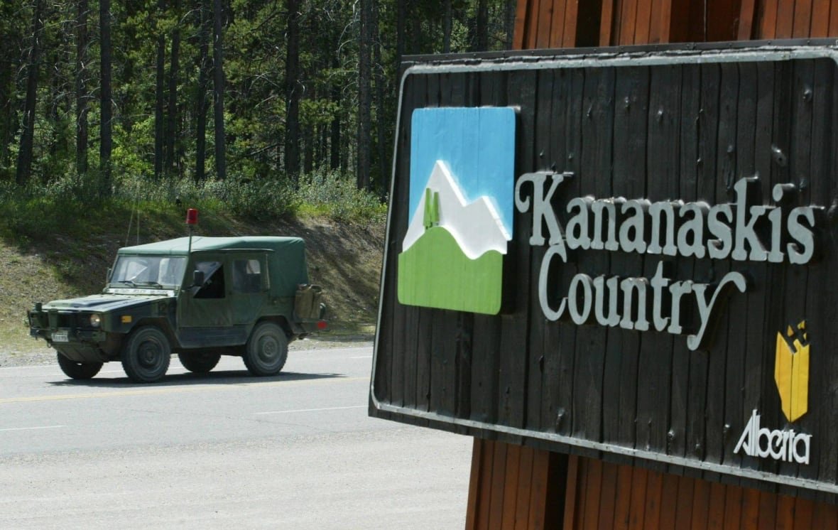A military vehicle drives down a road next to a sign that reads Kananaskis Country.