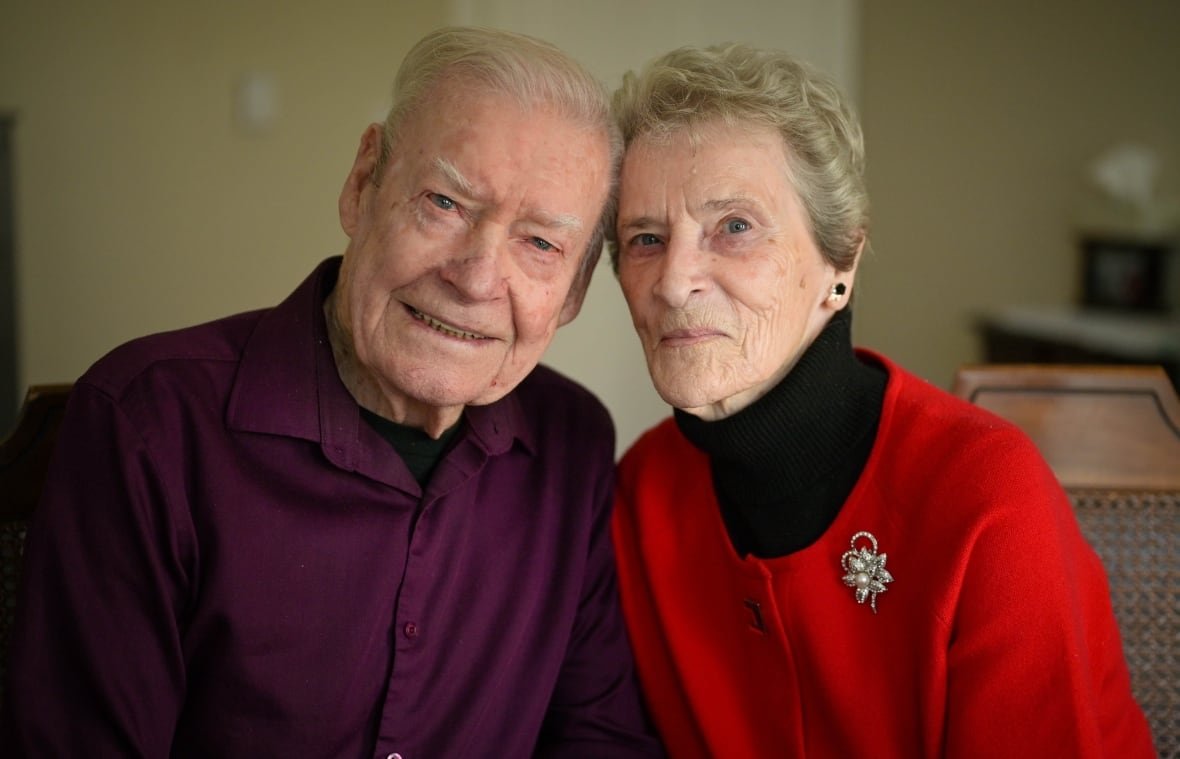 george-and-barbara-faulkner An elderly man and woman pose for the camera while leaning in close to one another.