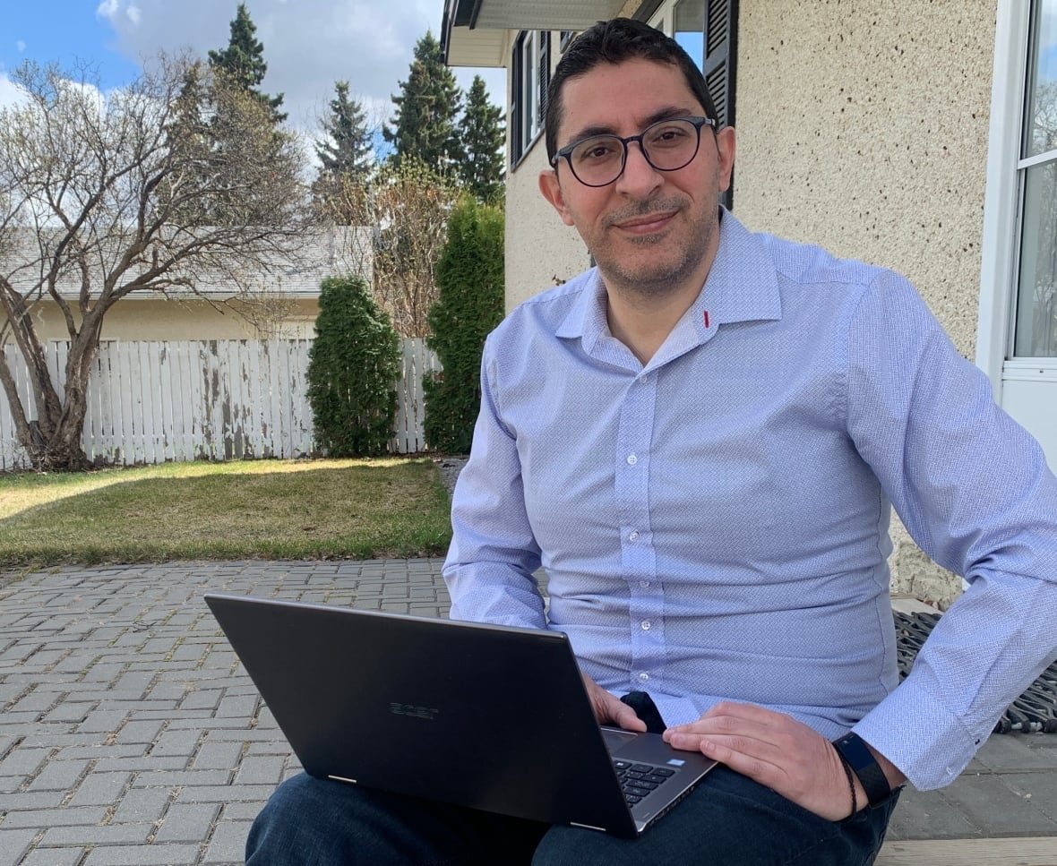 A man in a blue shirt sits on steps outside a building, with a laptop open on his lap.