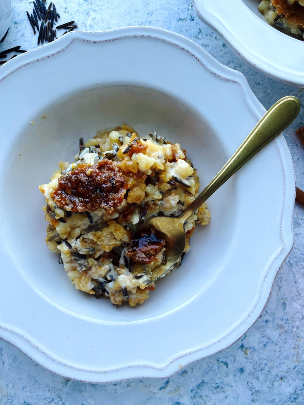 A spoon is seen dipped into a wild rice pudding on a white plate.