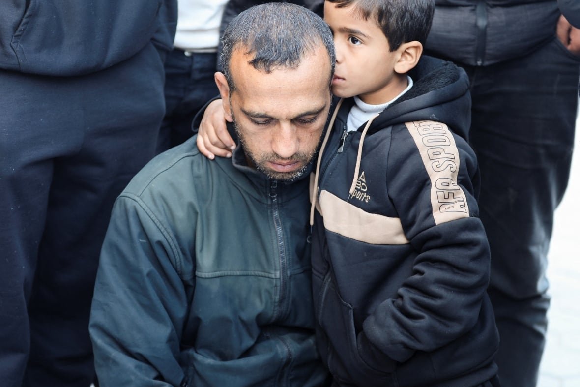 israel-palestinians-gaza-14 A boy embraces an older man, kissing the side of his head. Both look sad, and are in dark clothing.