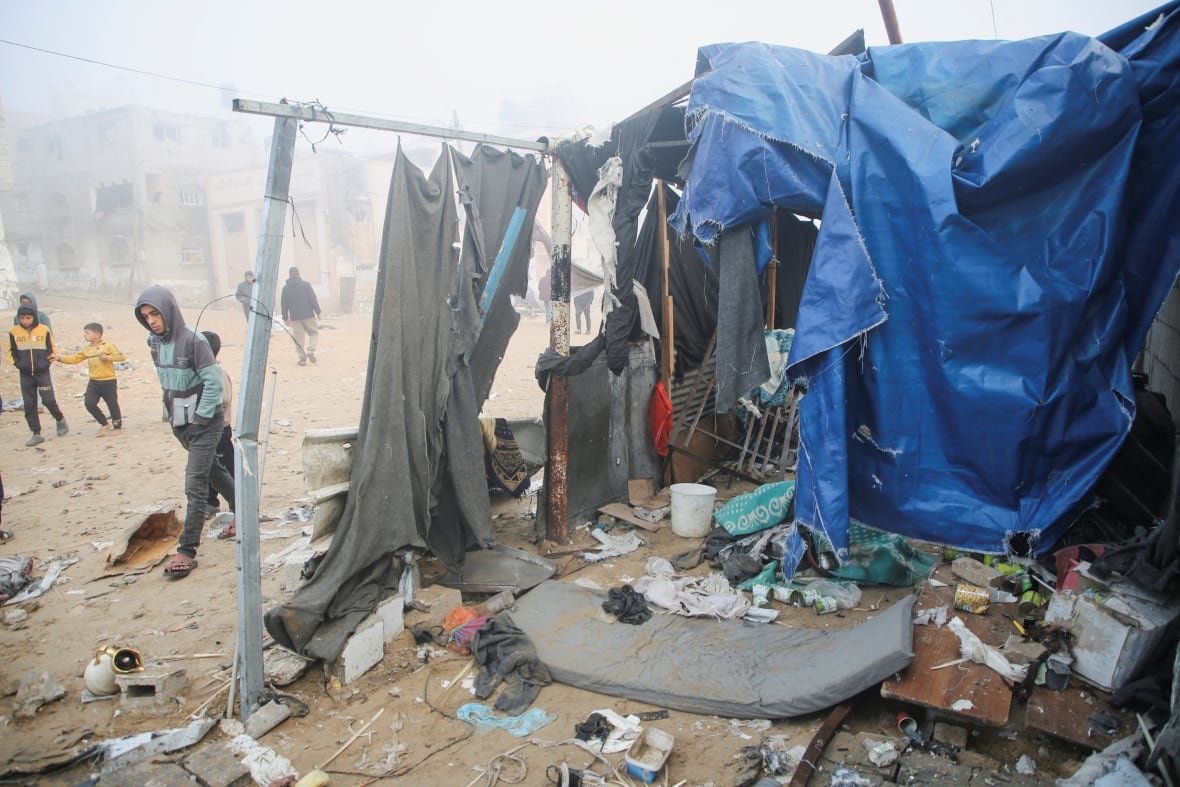 Debris and clothing is strewn on the ground near a tent, with kids shown walking around.
