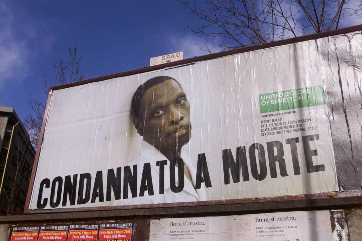 italy-sears-benetton-ads A billboard is shown in closeup. On it, an image of a cleanshaven, dark complected man is shown. He appears forlon. In Italian it reads Condannato A Morte, which translates to Condemned to Death.