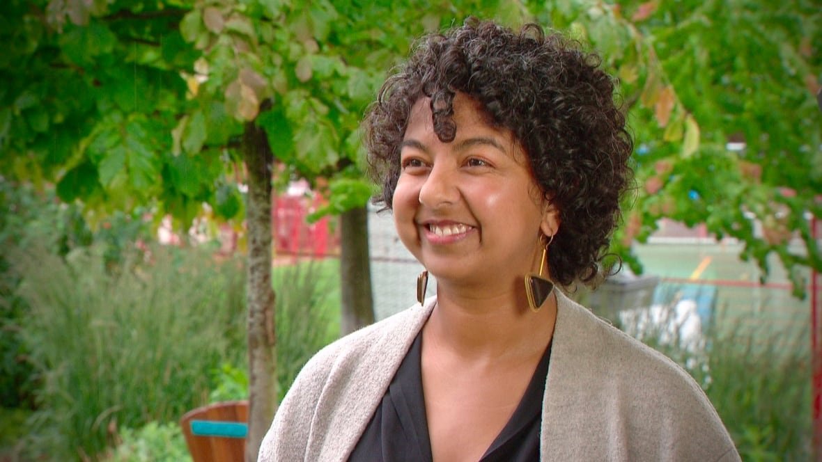 A woman with curly black hair smiles in a park environment.