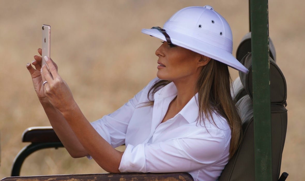 A woman in a white shirt and matching pith helmet takes a photo with a cel phone.