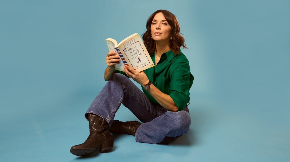 A Chilean woman wearing blue jeans, brown boots and a green blouse sits on the ground holding a beige book.