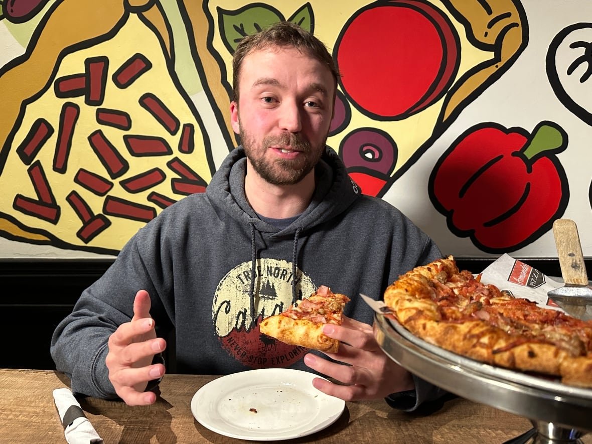 mike-zakoor-1 A man talks while holding a slice of pizza.