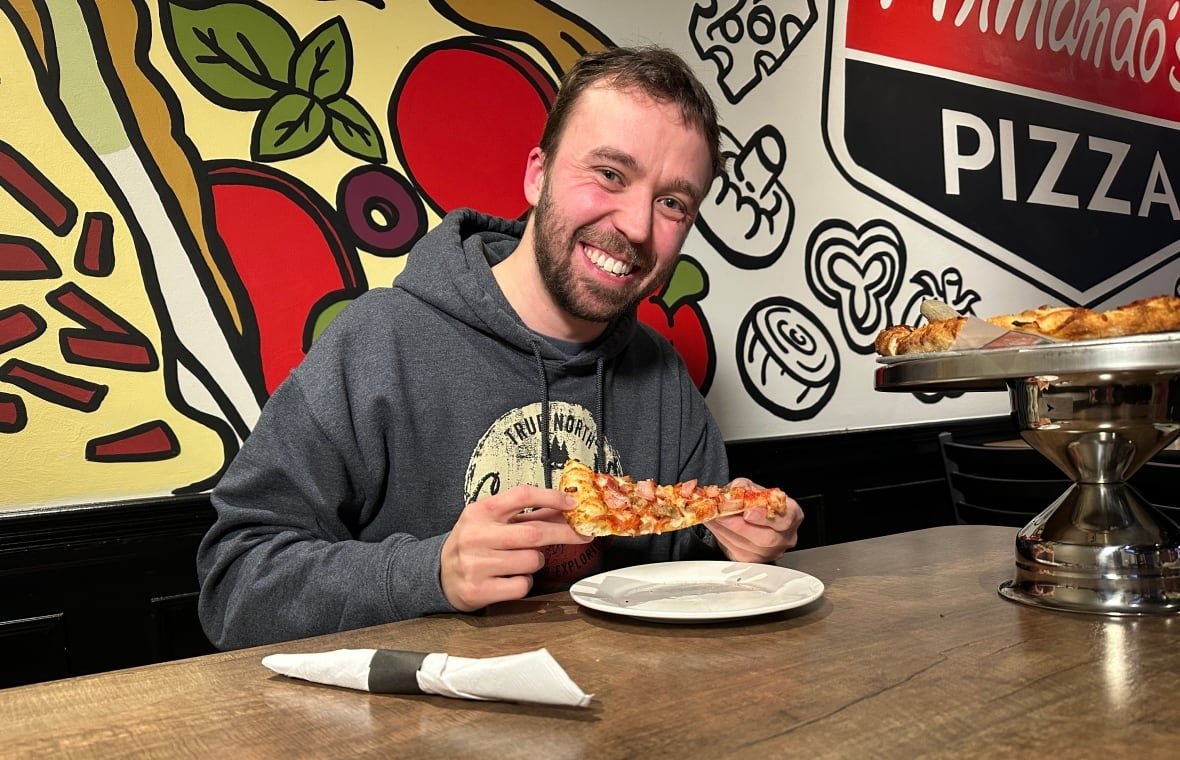 mike-zakoor-2 A man smiles holding a slice of pizza.