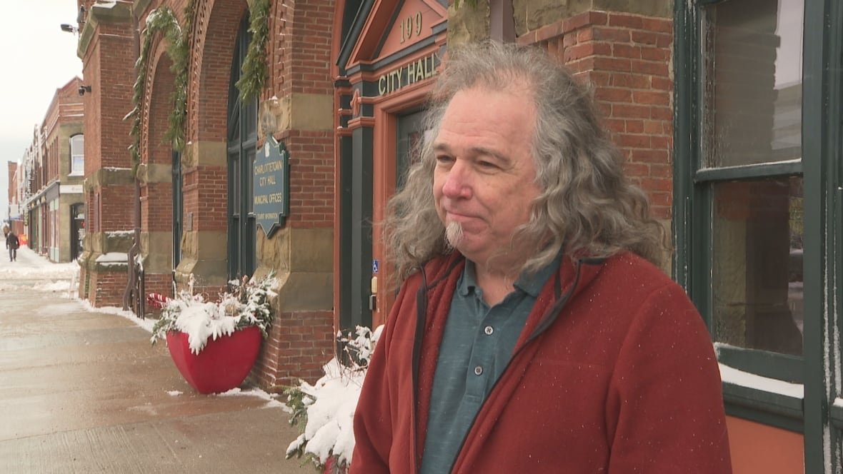 Paul Johnston stands outside City Hall wearing a red sweater.