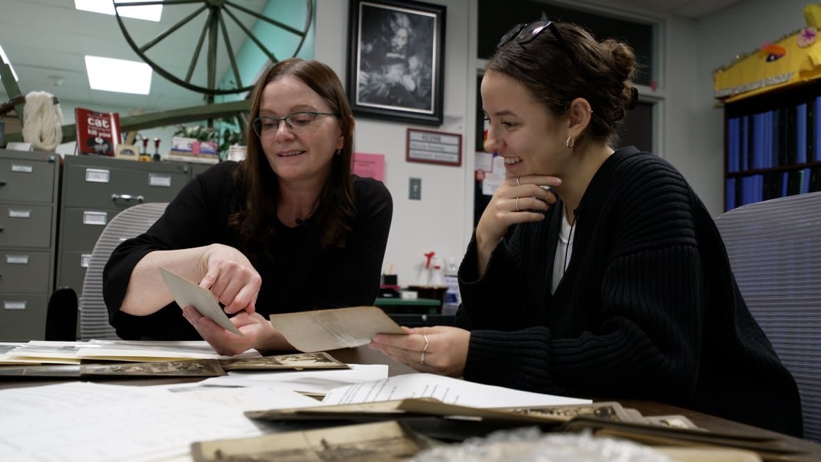 Two women look at a set of stereoscope cards.