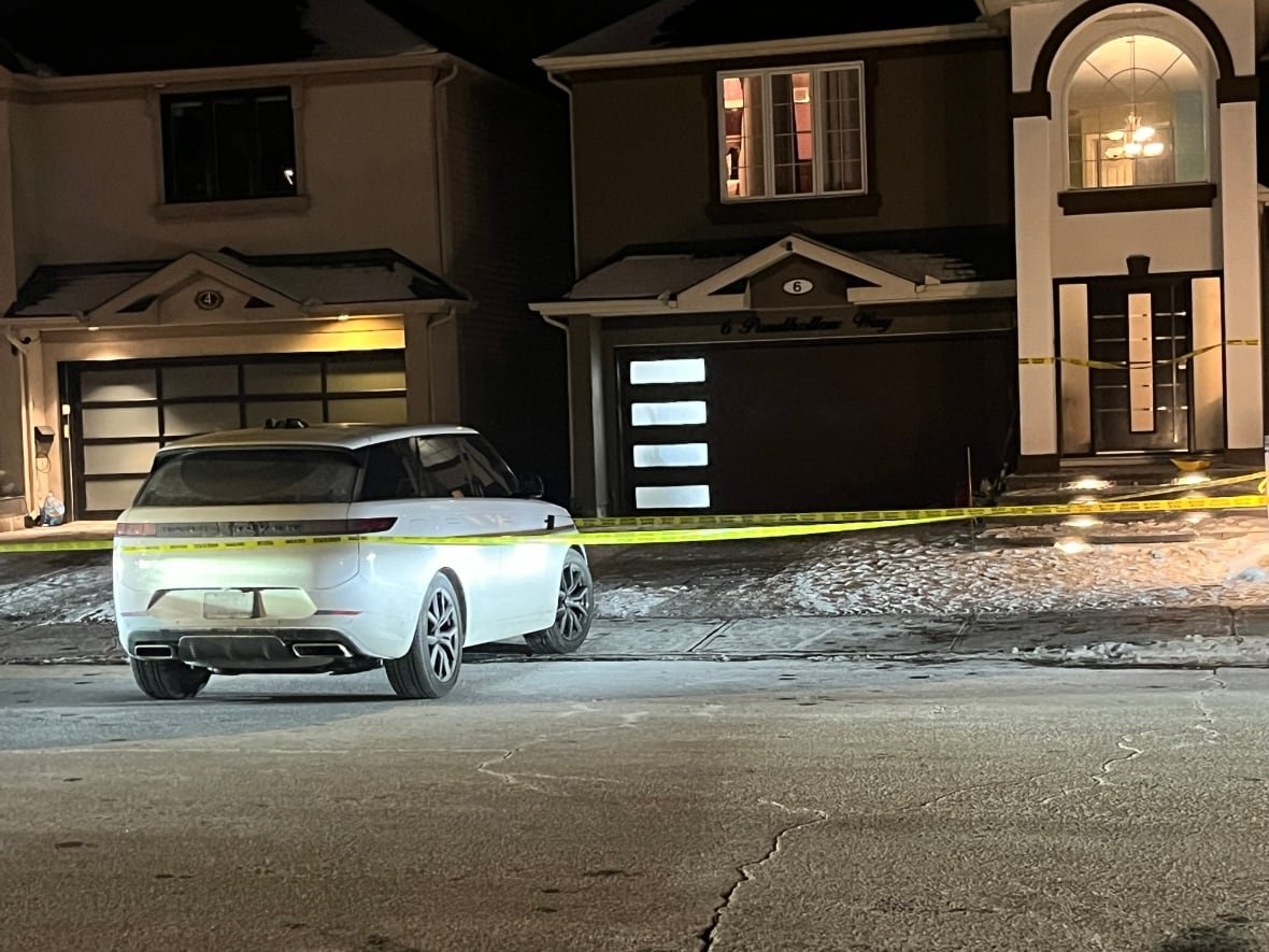 pondhollow-way-homicide-barrhaven-ottawa-police-service A suburban house at night with a white car halfway pulled out of the driveway with police tape surrounding it.