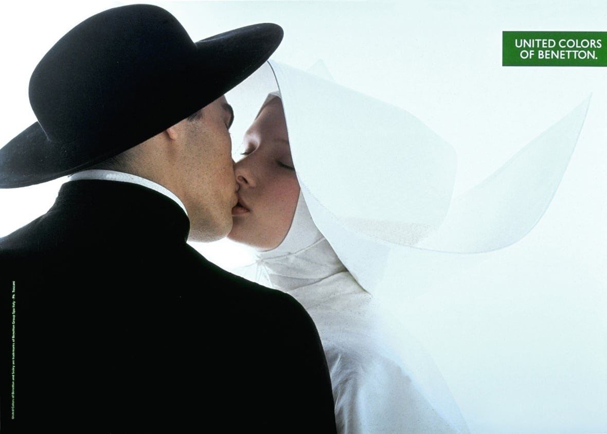 priest-and-nun-benetton-1991 A man in black kisses a woman in all-white. Both appear to be wearing religious garments.