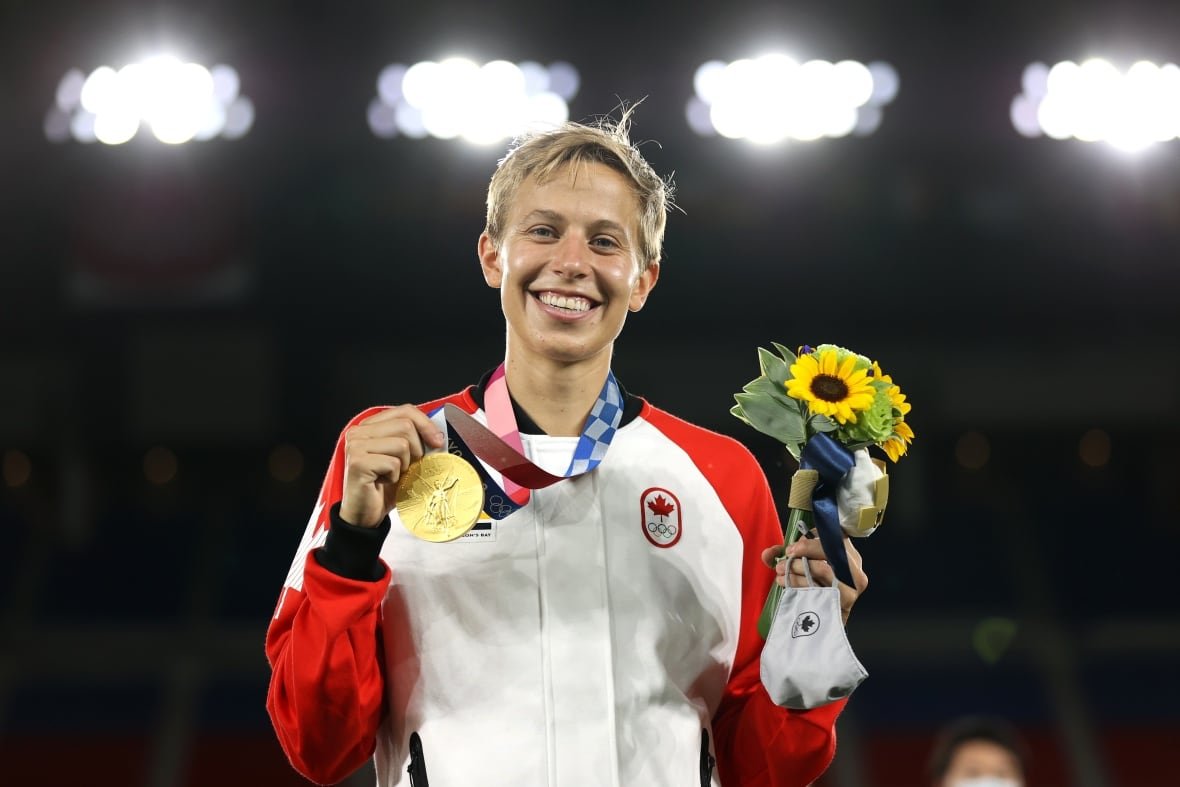 a person with short blonde hair holds flowers and a gold medal