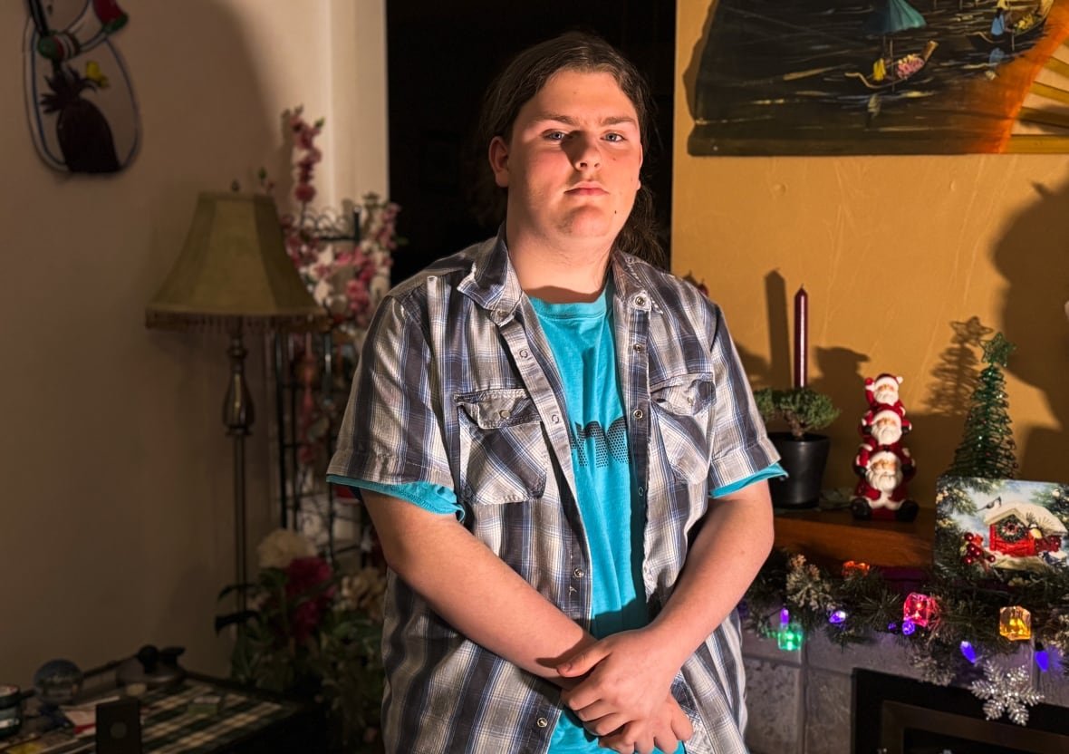 A young man stands in a home with with hands clasped in front of him.