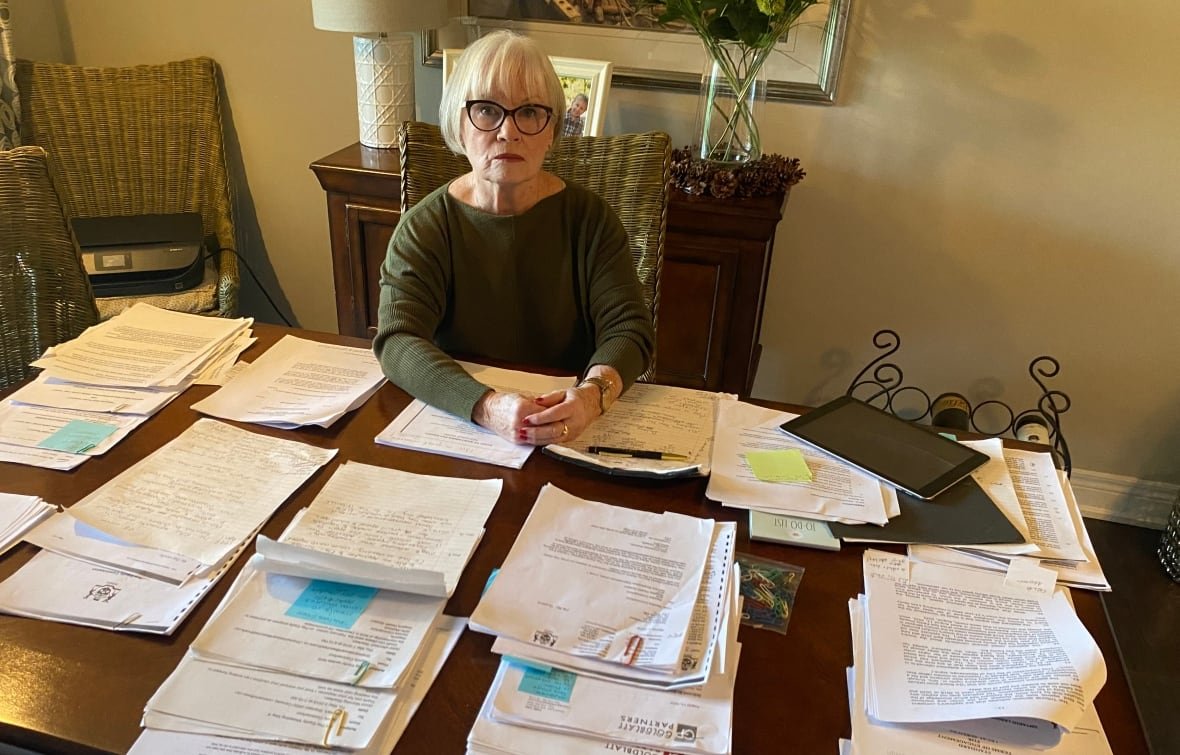sandra-commerford Woman sits at table with stacks of paper around her