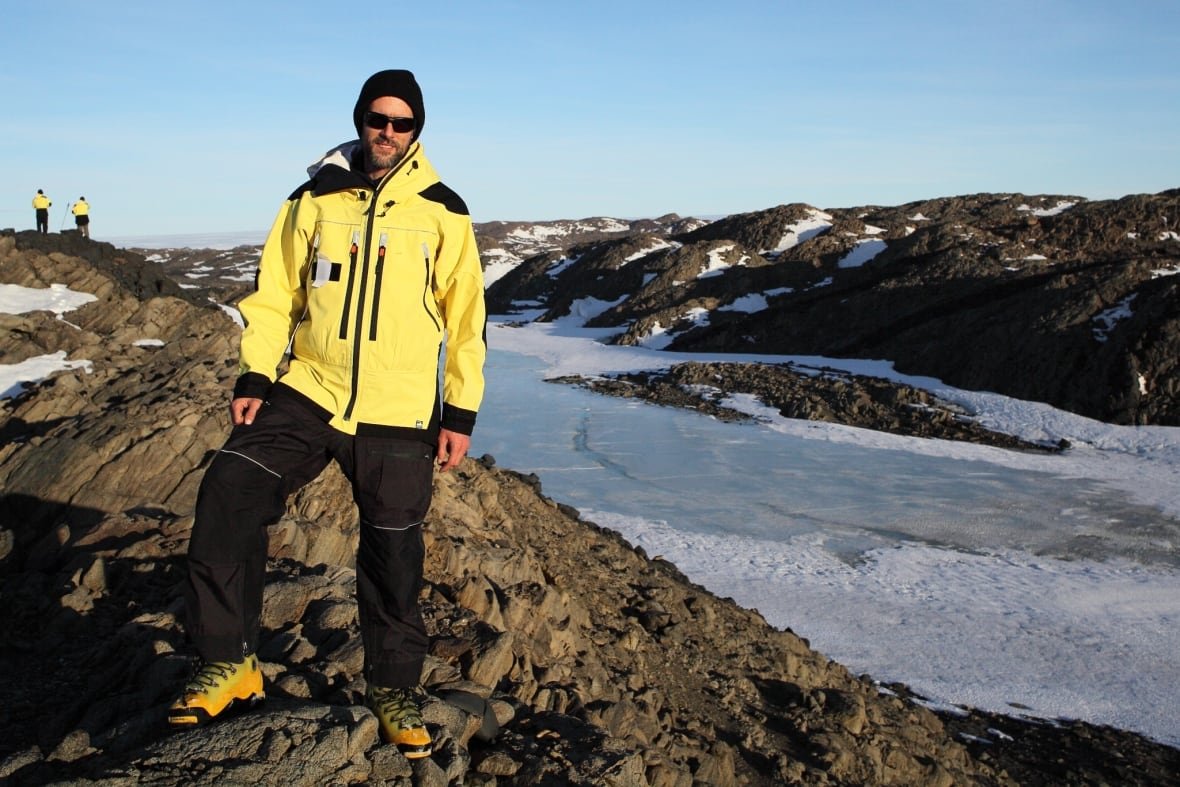 A man standing on an outdoor snowy, rocky terrain.