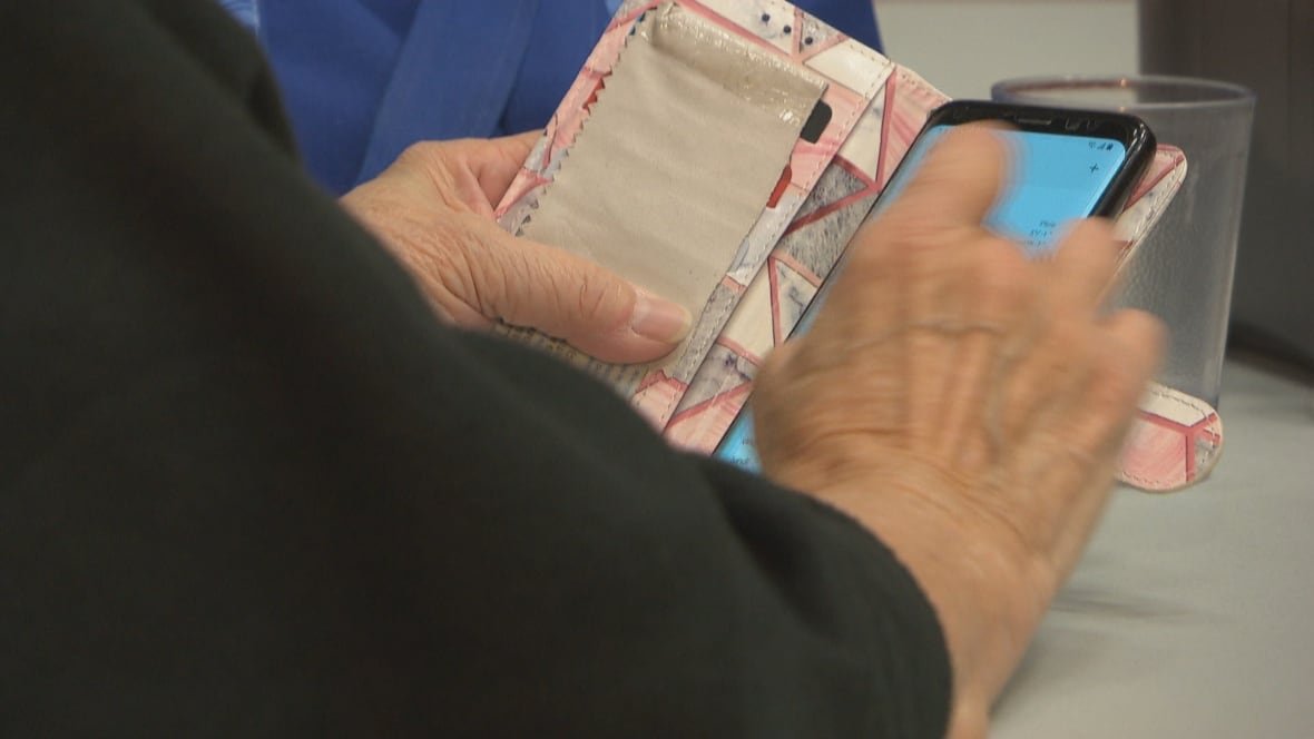 An elderly person holds a cellphone in her hand.