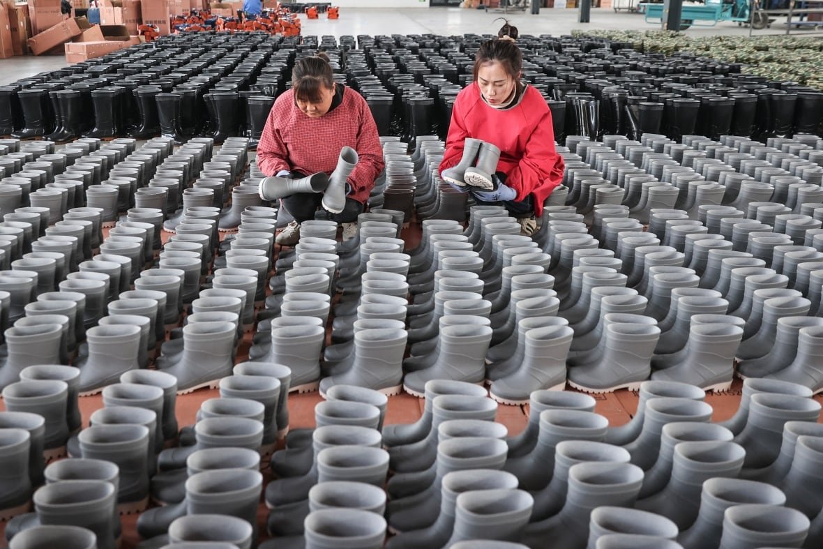 Women standing over tables filled with identical rain boots