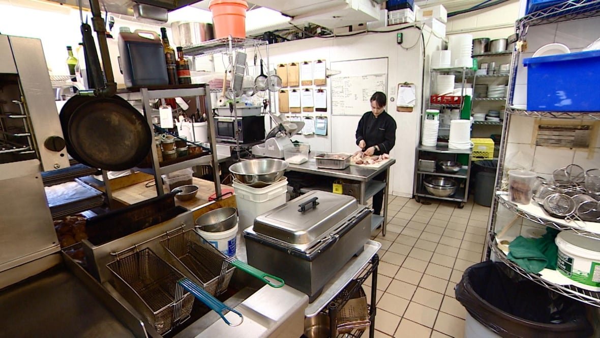 A photo taken inside of a restaurant kitchen that shows a chef cutting up meat.