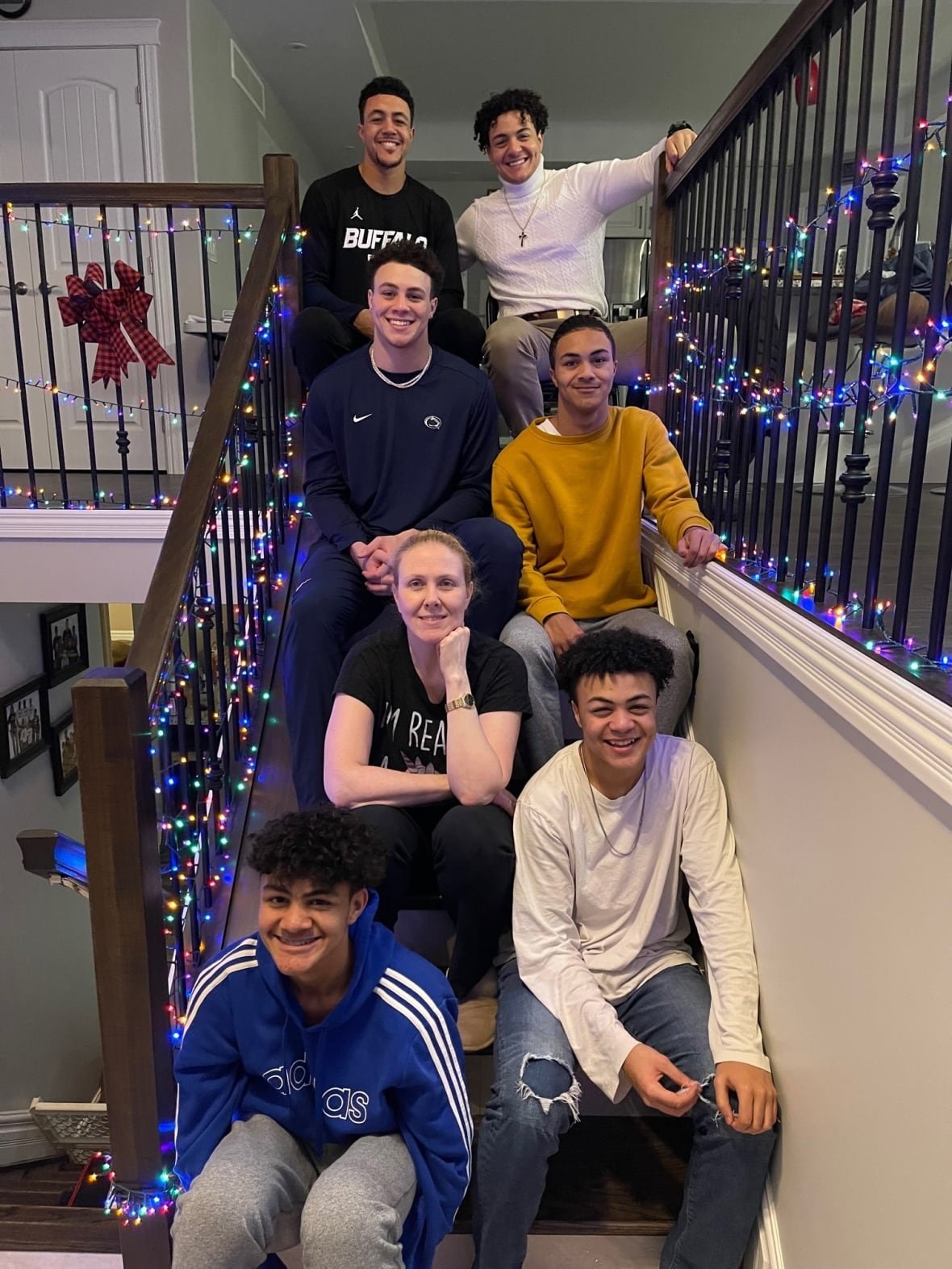theo-johnson-family Six boys sit with a woman, their mom, on the stairs with Christmas lights