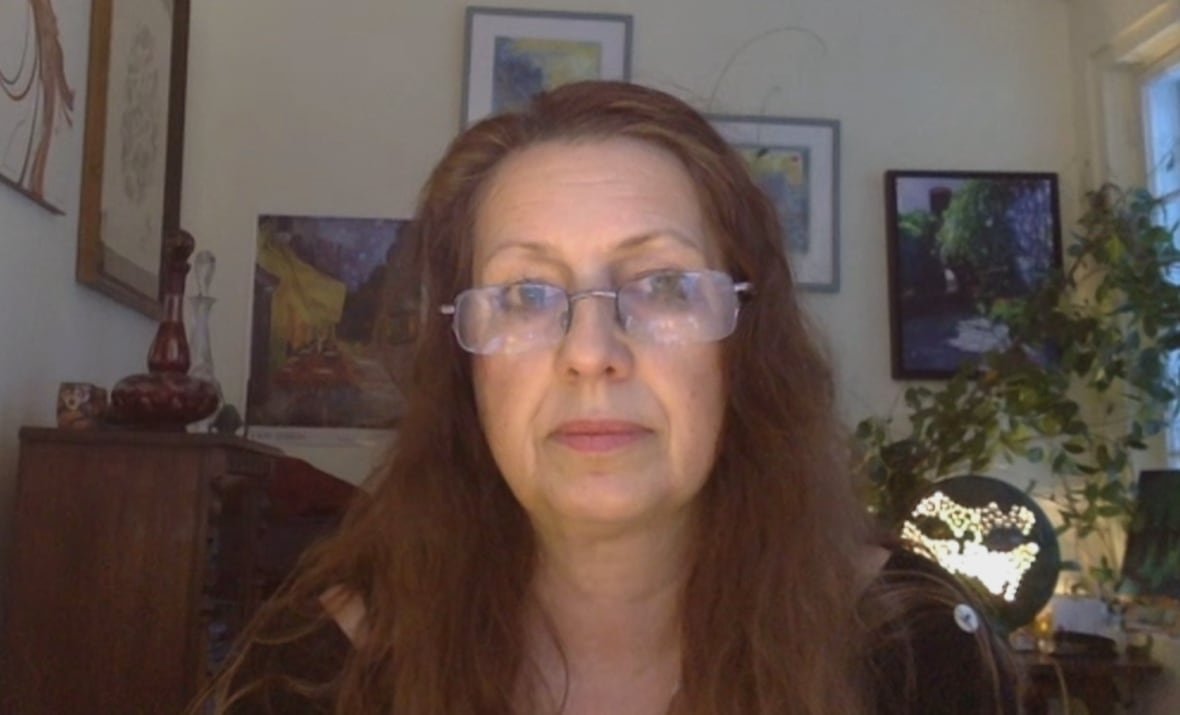 timea-spitka-carleton-university-ottawa-israel-ceasefire A woman with dark hair and frameless glasses looks into the camera. She is sitting in a room with picture frames and plants behind her.