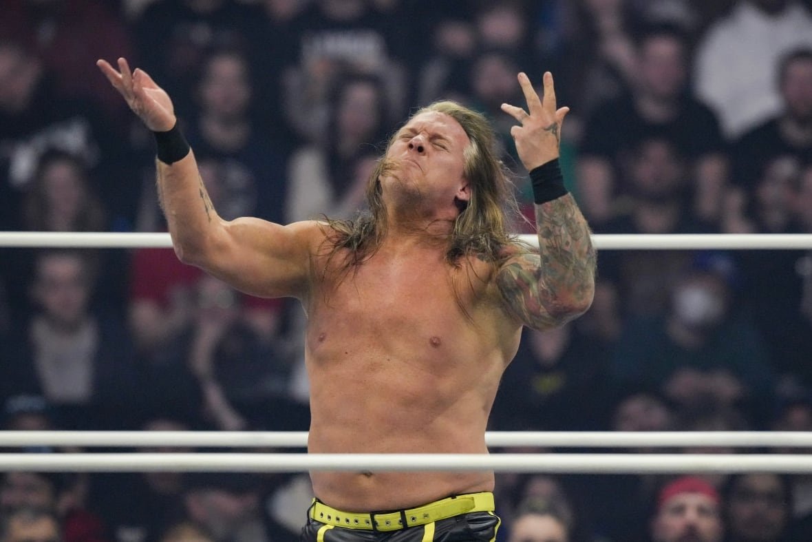 A wrestler with long hair gestures in the ring with his arms in front of his body
