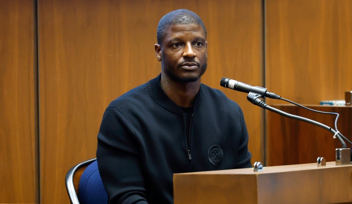 a-ap-rocky-shooting-trial-3 A man sits at a wooden podium with a microphone pointed at him.