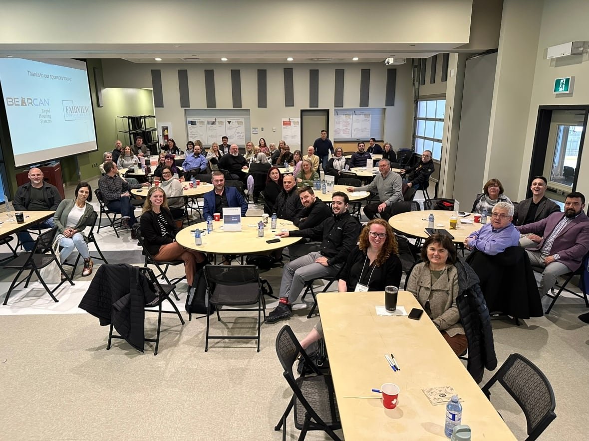 A large group of people sit at round tables in a large conference room.