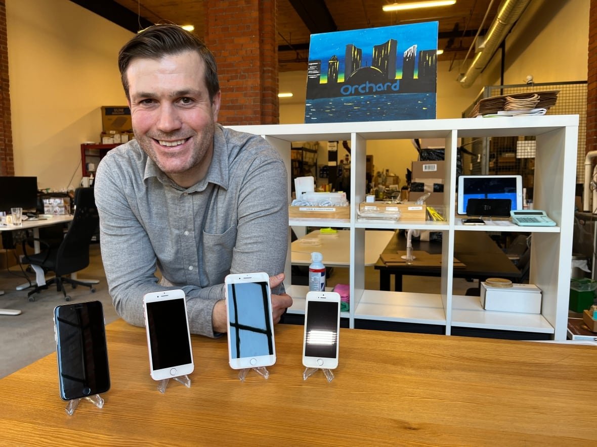 A man leans against a table where four iPhones are displayed.