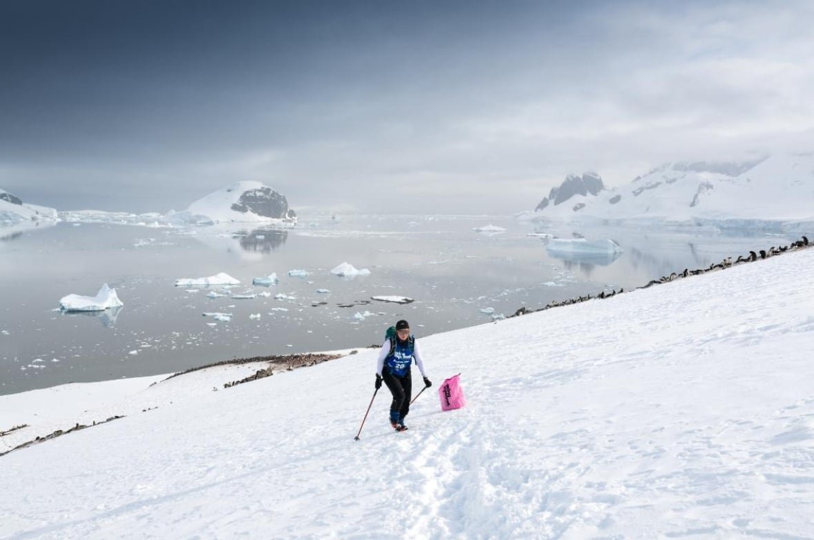 antarctic-marathon-2 A woman with ski poles moves through the snow, with arctic waters in the background.