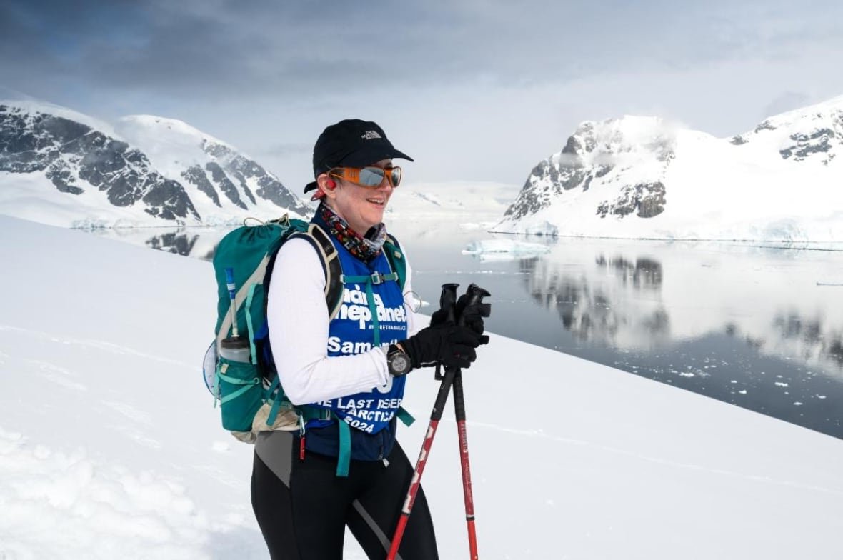 antarctic-marathon-3-1 A woman with ski poles stands in front of arctic water.