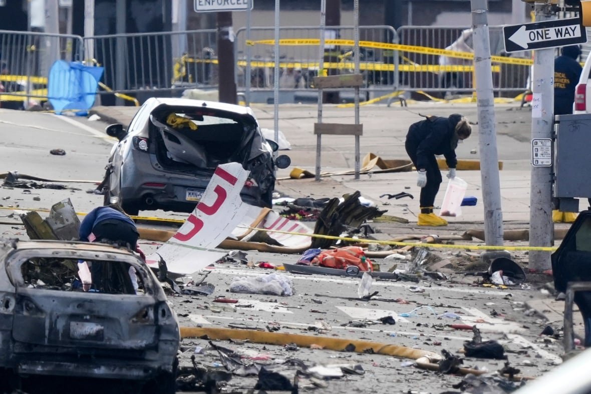 aptopix-philadelphia-small-plane-crash-1 A person collects aircraft wreckage on the street near damaged cars.